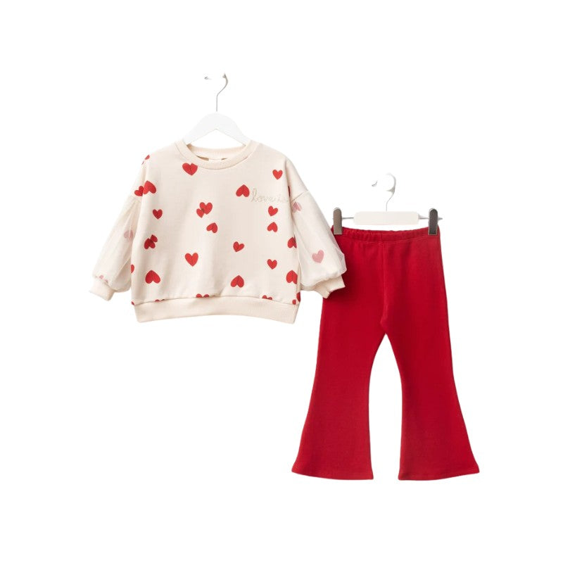 A children's two-piece outfit set featuring a cream-colored long-sleeve sweatshirt with red heart prints and matching red flared pants, displayed on white hangers against a plain white background.