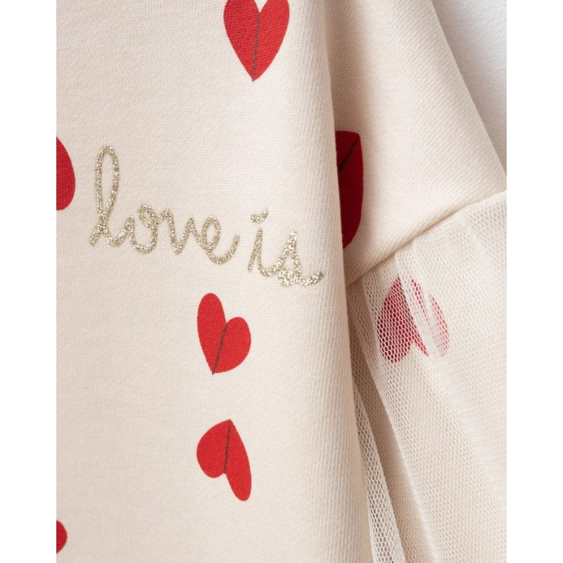 Close-up of a cream-colored fabric garment with red heart prints and glittery gold cursive text reading 'love is'.