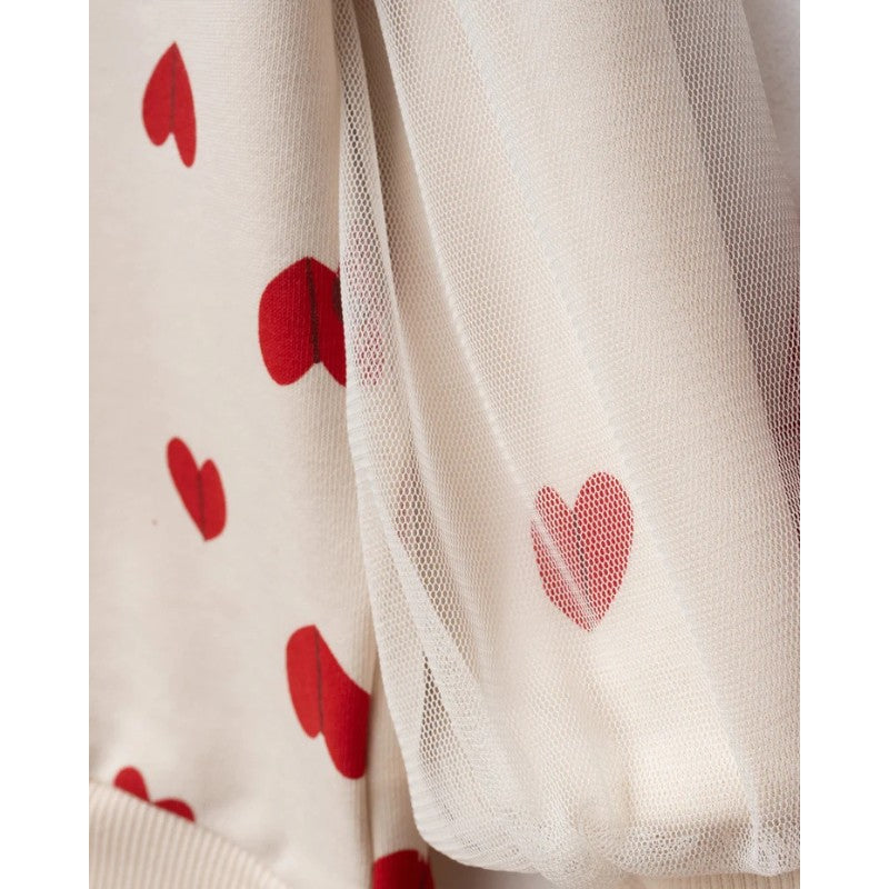 Close-up of a cream-colored fabric garment with red heart prints and a sheer white mesh overlay.