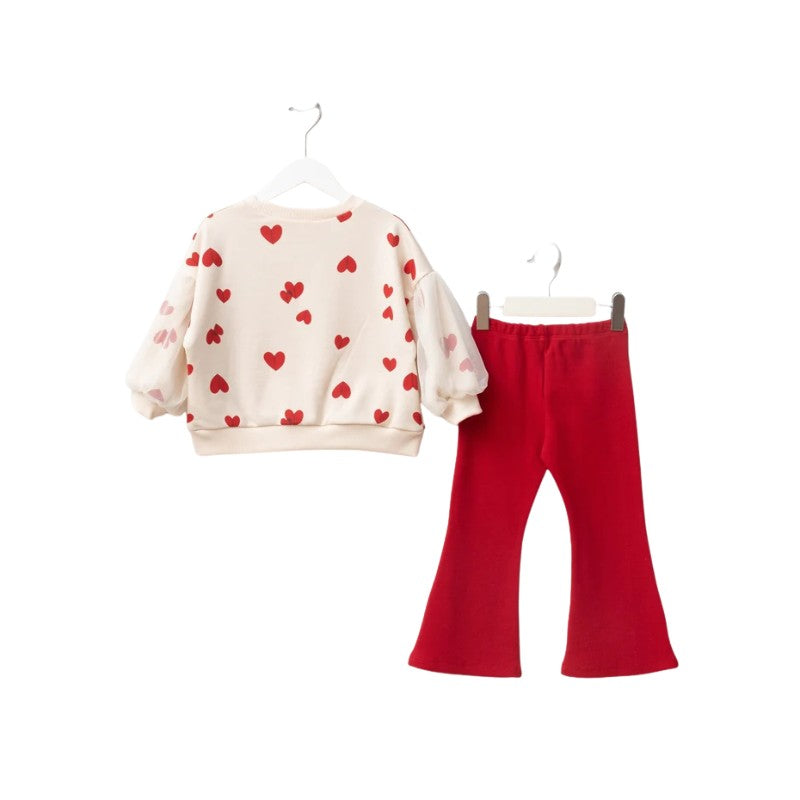 A two-piece children's outfit set featuring a cream-colored sweatshirt with red heart patterns and sheer puff sleeves, paired with bright red flared pants, shown on hangers against a white background.