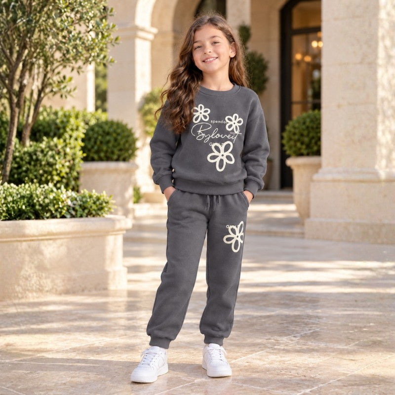 Girl wearing a grey floral sweatshirt and matching joggers with white trainers in a stone courtyard.