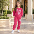 Girl wearing a pink floral sweatshirt and matching joggers with white trainers in a stone courtyard.