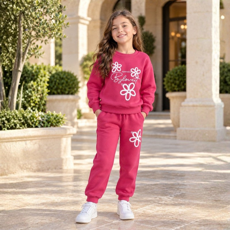 Girl wearing a pink floral sweatshirt and matching joggers with white trainers in a stone courtyard.