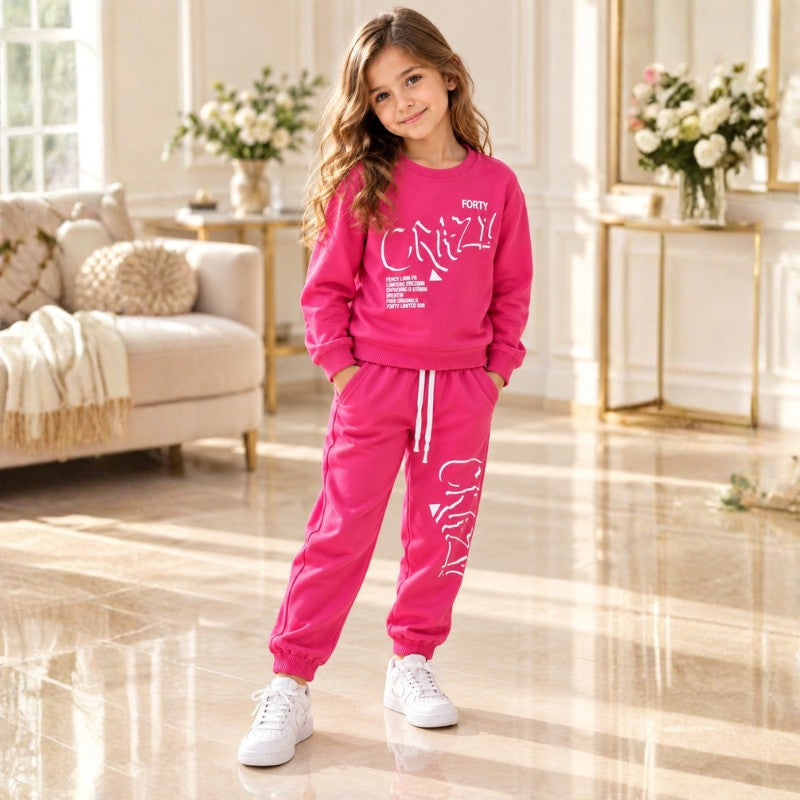 Girl wearing a bright pink graphic sweatshirt and matching joggers with white trainers.