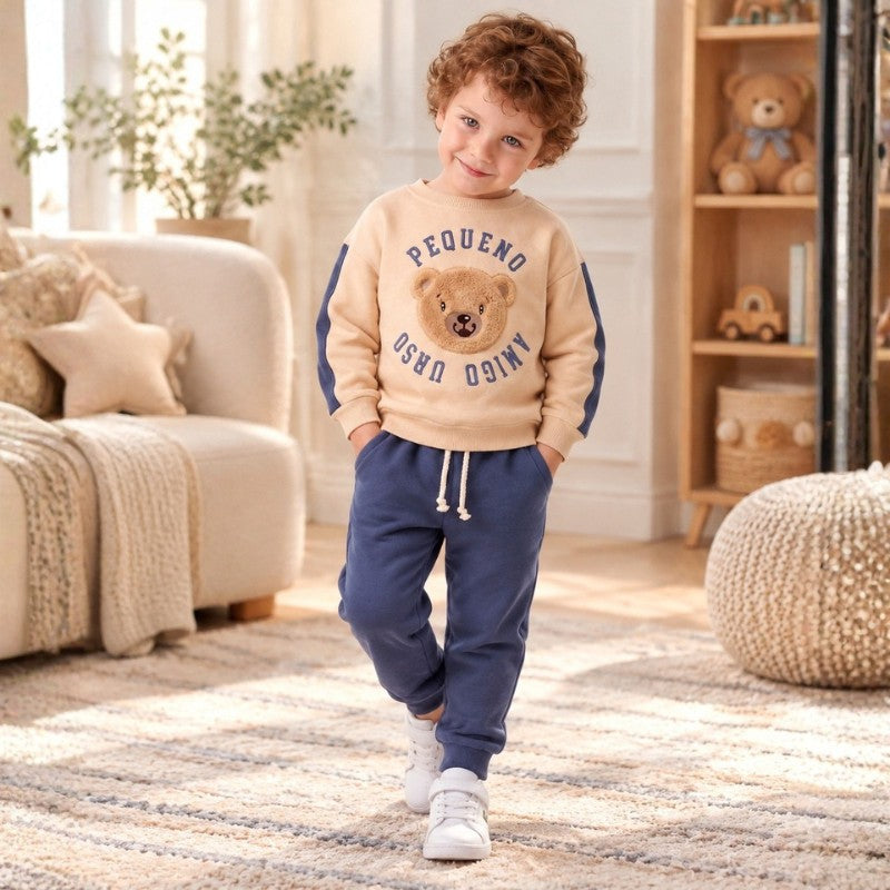 Child wearing a beige teddy bear sweatshirt with blue sleeve accents and matching blue joggers