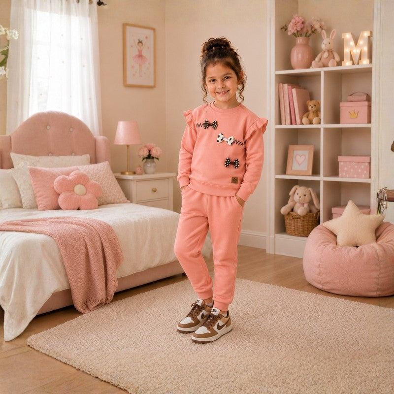 Girl wearing a peach pink bow-detail sweatshirt and matching jogger pants tracksuit set