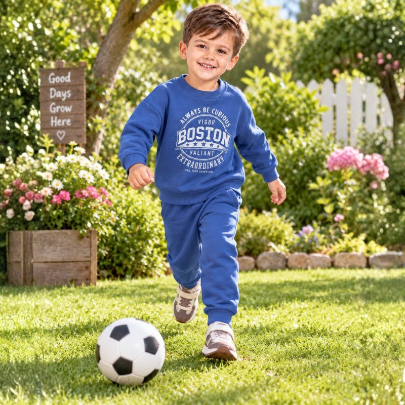 Young boy wearing a blue Boston graphic sweatshirt with matching jogger pants, a comfortable kids casual tracksuit for outdoor play