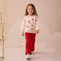 Girl wearing an ivory heart print top with sheer puff sleeves and red flared pants