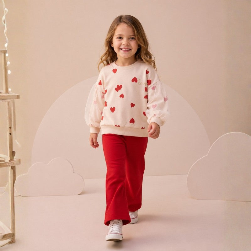 Girl wearing an ivory heart print top with sheer puff sleeves and red flared pants