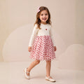 Girl wearing an ivory long-sleeve dress with a pink heart-print tulle skirt and matching bow hair accessory