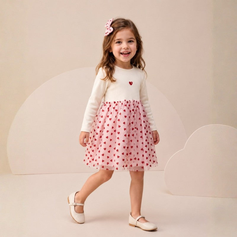 Girl wearing an ivory long-sleeve dress with a pink heart-print tulle skirt and matching bow hair accessory