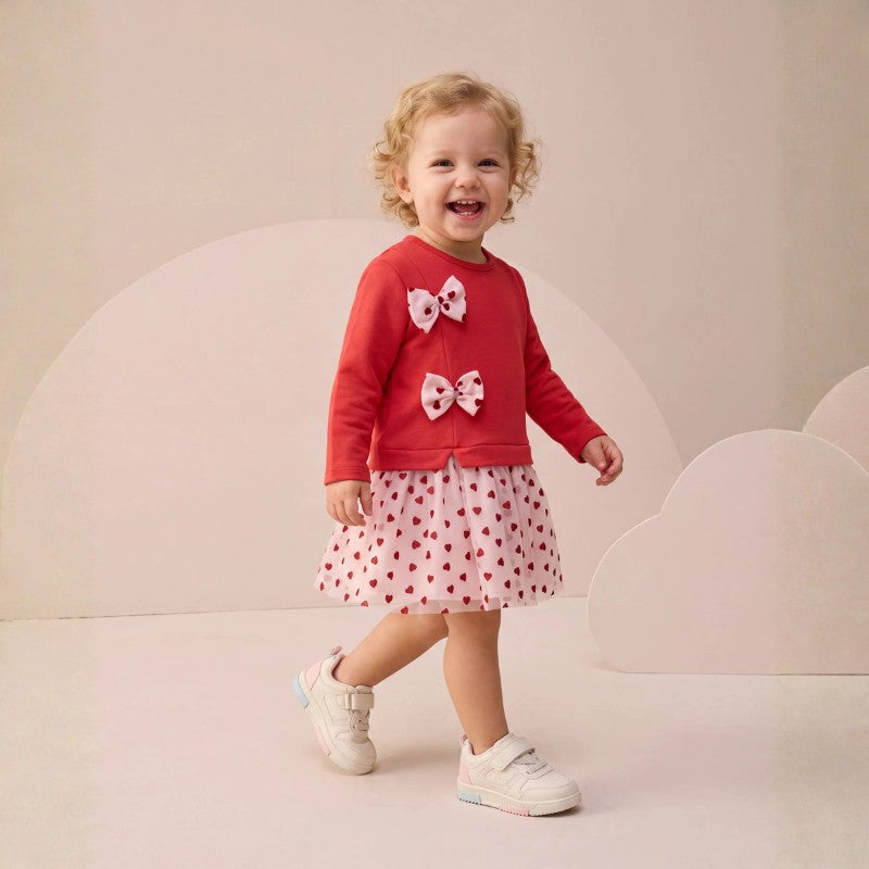 Toddler girl wearing a long-sleeve dress with bow details and a red heart-print tulle skirt