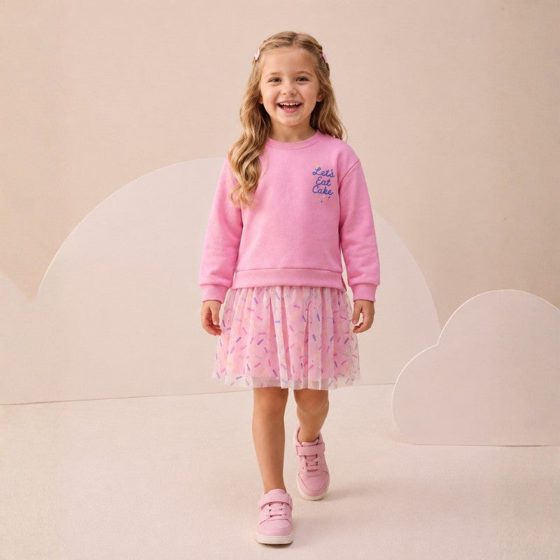 Girl wearing a long-sleeve dress with “Let’s Eat Cake” print and a tulle skirt