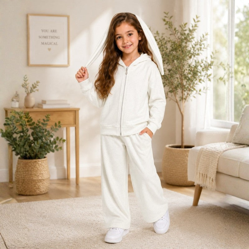 Young girl wearing a white bunny-ear hoodie tracksuit set in a bright cozy room.