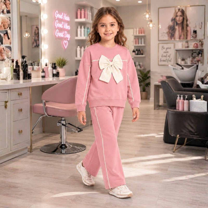 Girl wearing a pink sweatshirt with an oversized bow and matching wide-leg pants, stylish children's two-piece casual outfit