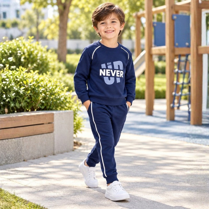 Young boy wearing a navy Never Give Up sweatshirt with matching jogger pants and sporty side stripes, a casual kids tracksuit set