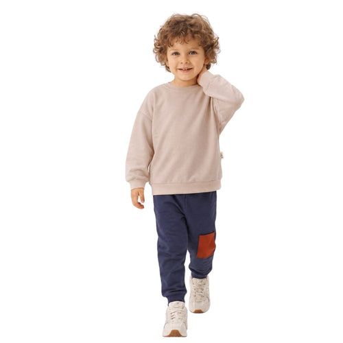 Young boy wearing a taupe sweatshirt with navy jogger pants featuring a patch pocket 