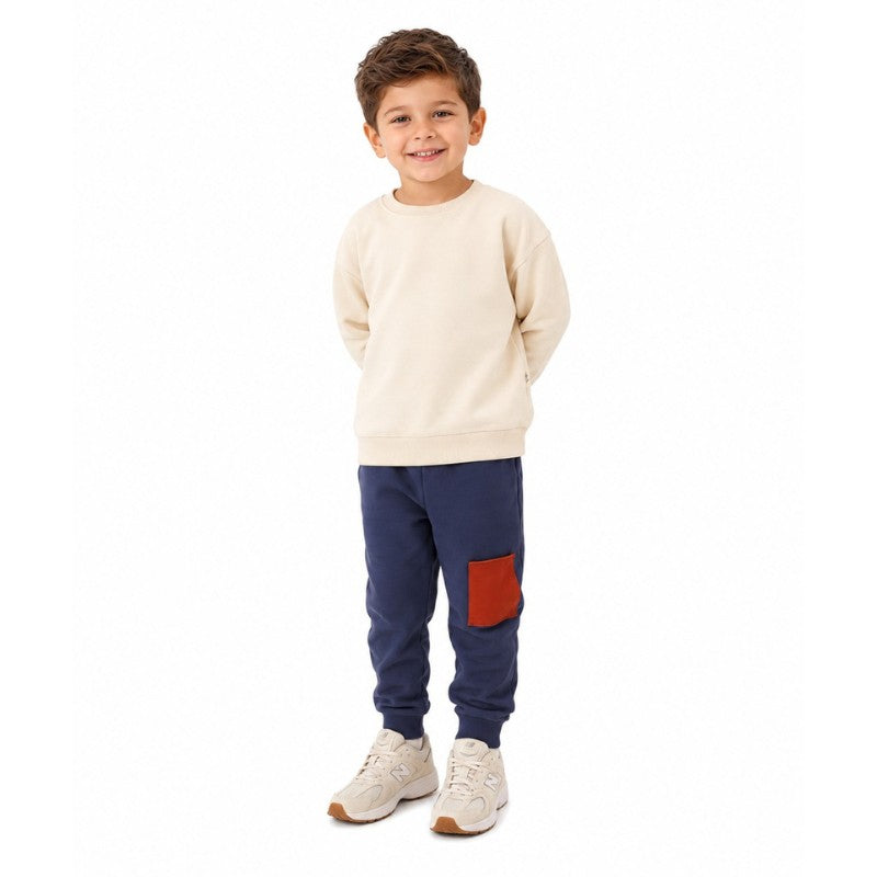 Young boy wearing a taupe sweatshirt with navy jogger pants featuring a patch pocket