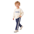 Young boy wearing a cream “Snacks” sweatshirt and pants with white side stripes