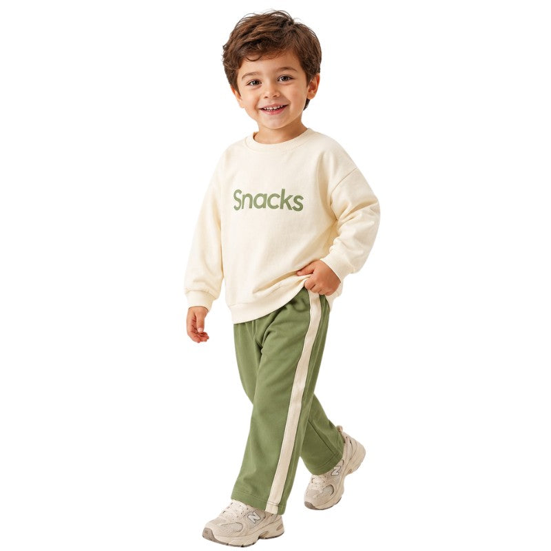 Young boy wearing a cream “Snacks” sweatshirt and pants with white side stripes