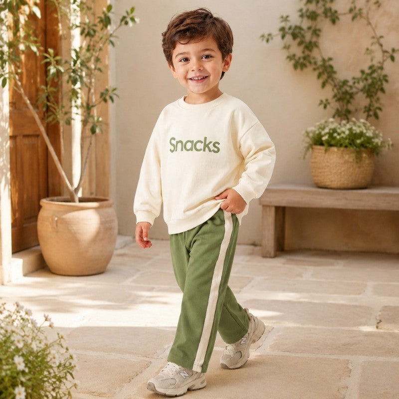 Young boy wearing a cream “Snacks” sweatshirt and pants with side stripes