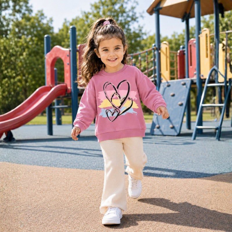 Young girl wearing a pink heart-print sweatshirt and cream pants