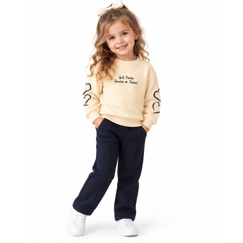 Young girl wearing a butter-yellow slogan sweatshirt with navy heart-print sleeves, matching navy joggers 
