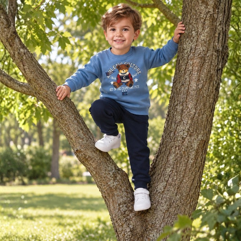 Young boy wearing a light blue teddy bear sweatshirt and navy pants climbing a tree outdoors