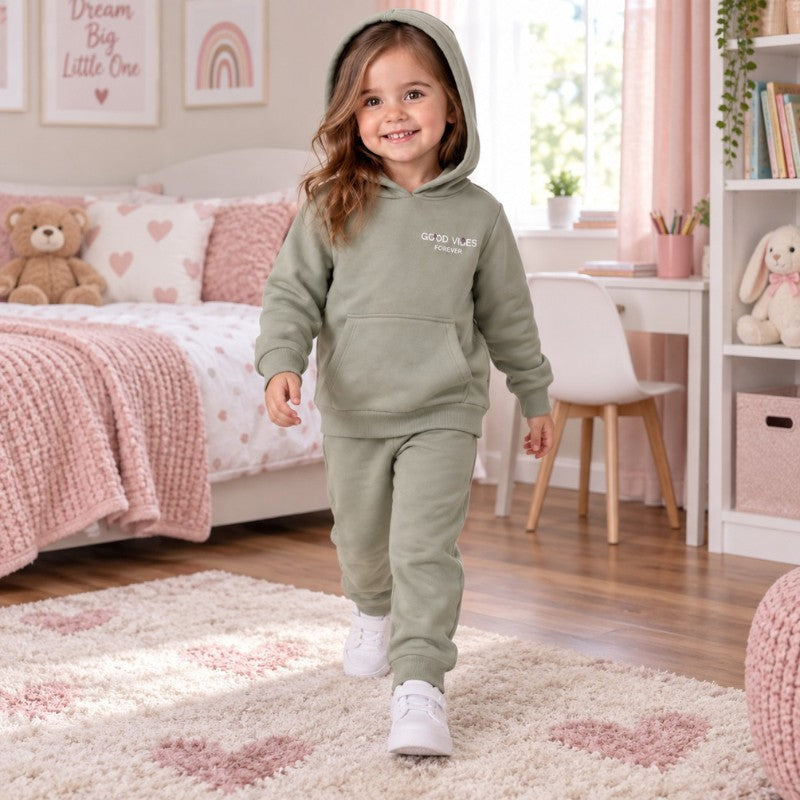 Young girl wearing a sage green slogan hoodie with a kangaroo pocket and matching cuffed joggers.