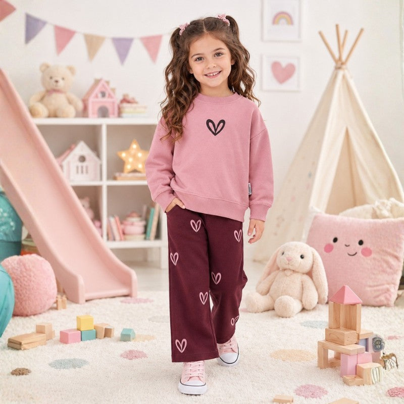 Young girl wearing a sweatshirt with a heart graphic and jogger pants featuring pink heart prints, stylish children's two-piece outfit.