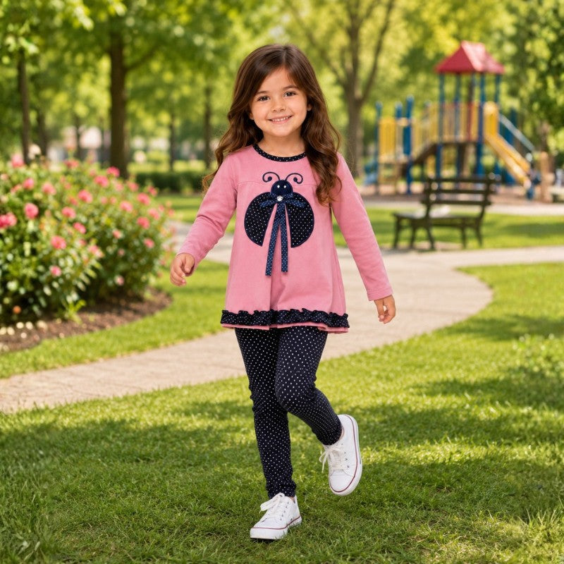 Young girl wearing a pink ladybug tunic with navy polka-dot leggings and white sneakers while walking in a park.