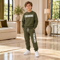 Boy wearing an olive TREMORS sweatshirt and matching joggers with white trainers in an elegant cream interior.