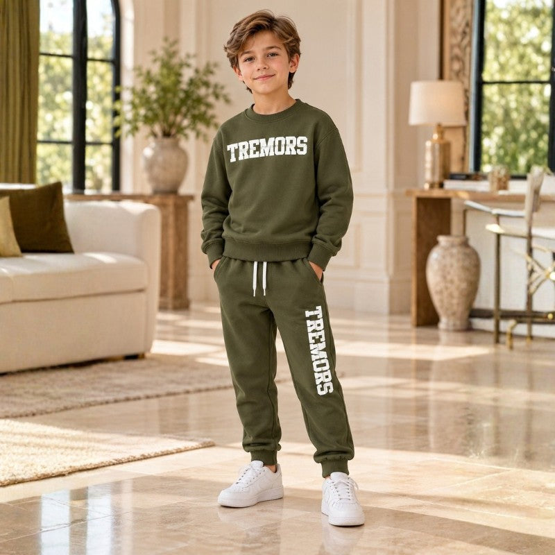 Boy wearing an olive TREMORS sweatshirt and matching joggers with white trainers in an elegant cream interior.