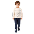 Young boy wearing a cream graphic sweatshirt and jogger pants.